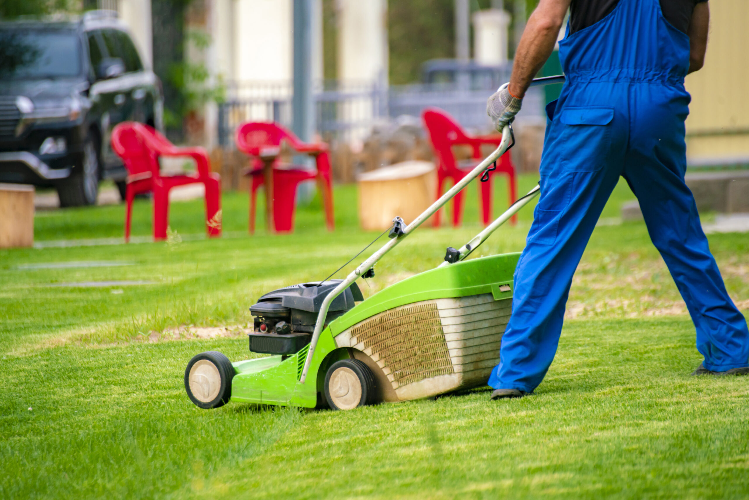 gardener worker cutting grass with mower in the backyard lawn field