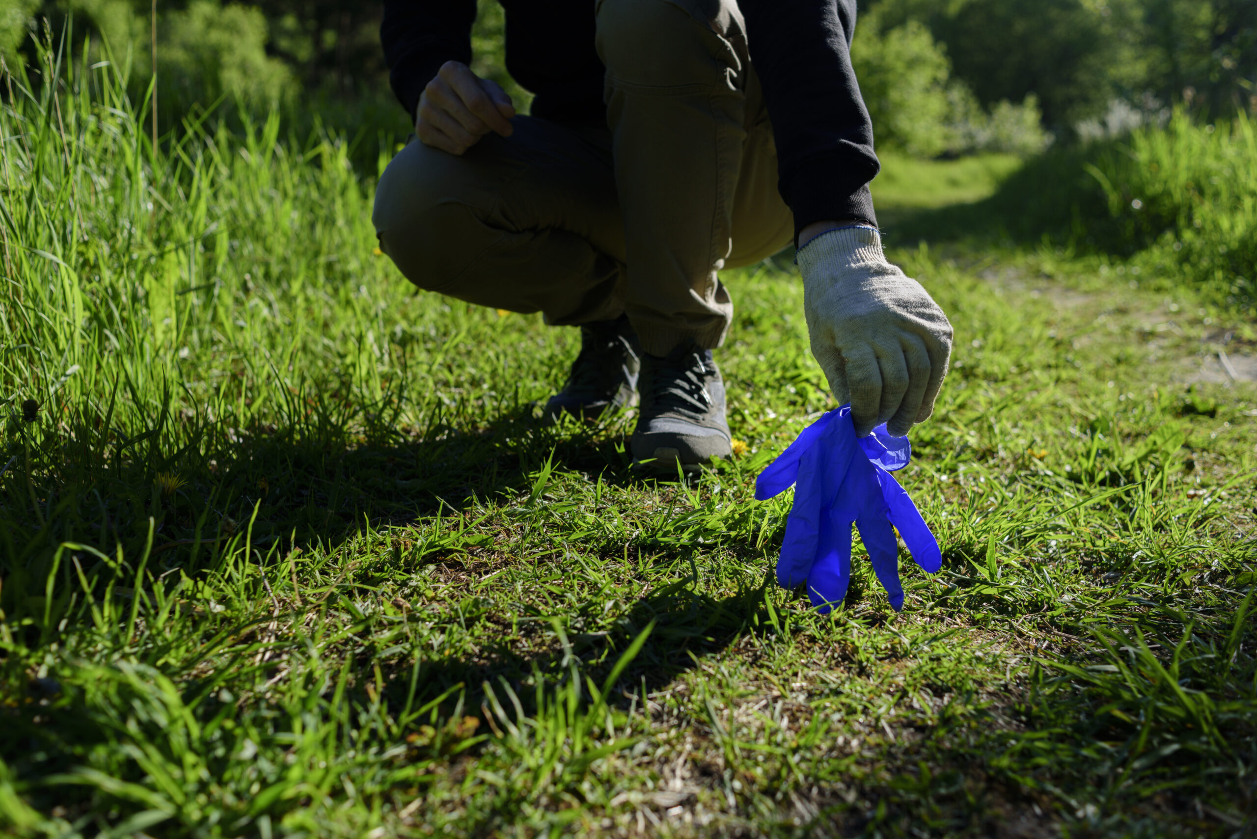 Man holding used disposable medical gloves in forest. Pollution due coronavirus pandemic